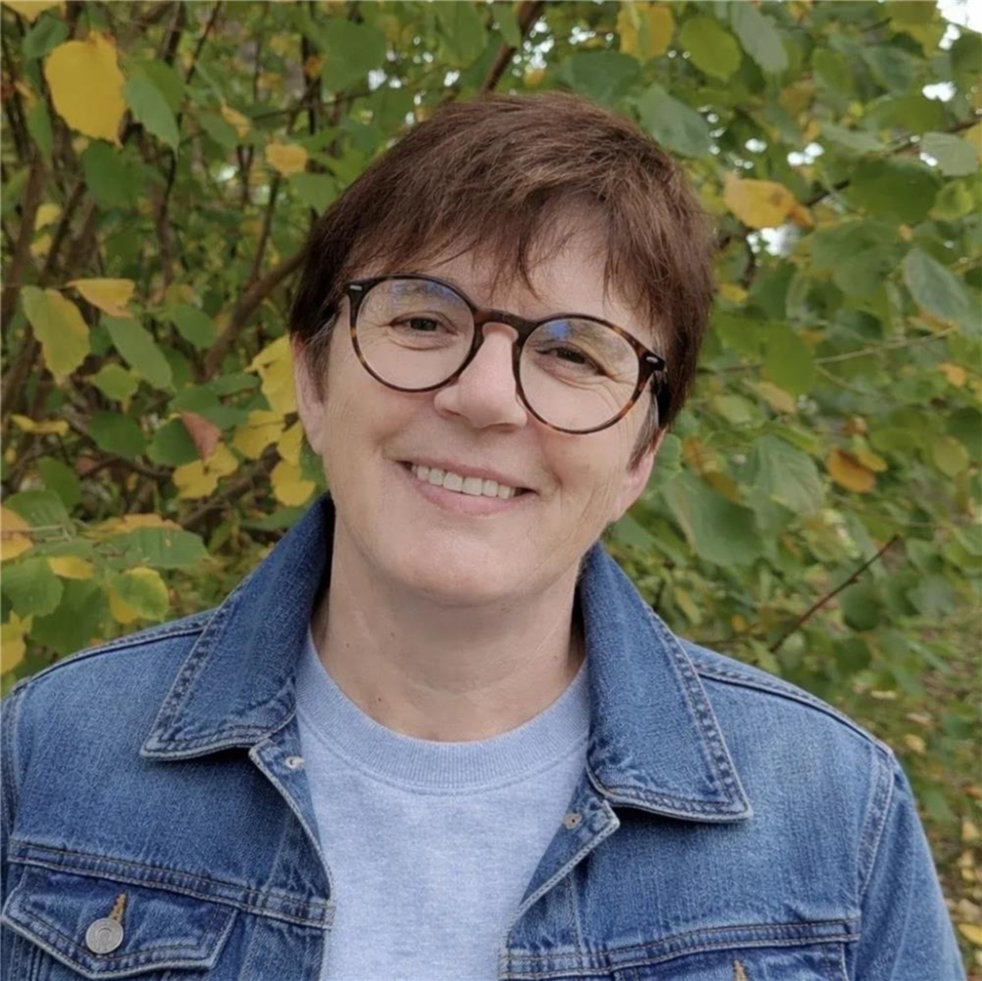 Eine Frau steht vor einem Busch. Sie lächelt.