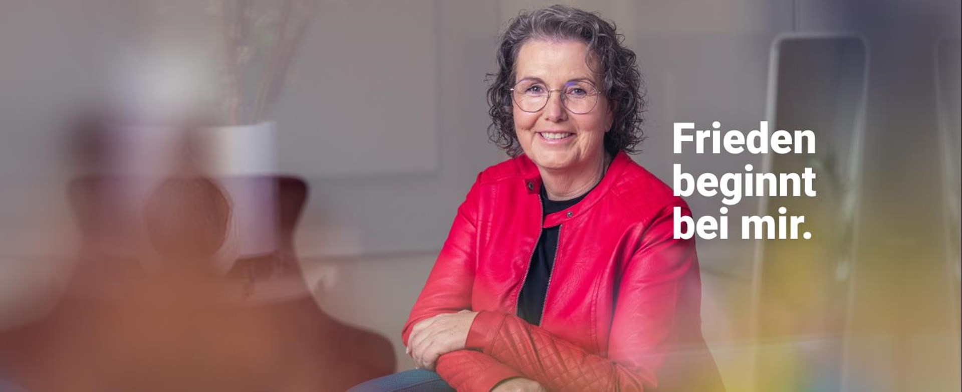 Eine Frau mit grauen gelockten Haaren und Brille mit der Aufschrift "Frieden beginnt bei mir."